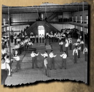 Carlisle Students in School Uniform Exercising Inside Gymnasium; Some with Indian Clubs, Others with Gymnastic Equipment; Non-Native Group Watching, 1879.